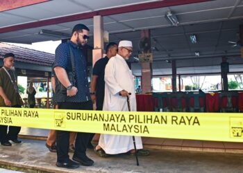 ABDUL Hadi Awang (depan) diiringi pegawai memasuki tempat mengundi di SK Rusila, Marang, hari ini. - UTUSAN/PUQTRA HAIRRY ROSLI