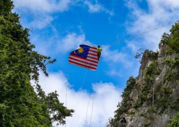 MUHAMMAD Amirul Baharti,32, bersama komuniti Perlis Climber dalam keadaan terapung memasang Jalur Gemilang disebalik awan biru diantara laluan dua bukit di Bukit Keteri, Chuping, Perlis semalam.- UTUSAN/SHAHIR NOORDIN