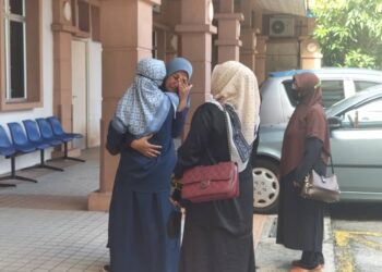 NURAINI Mohamad Isa mengesat air matanya ketika dipeluk oleh seorang ahli keluarga di pekarangan Jabatan Perubatan Forensik, Hospital Pulau Pinang (HPP), hari ini.-UTUSAN/SAFINA RAMLI