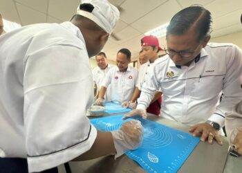 AZMAN Adnan (kanan) melihat seorang pelajar membuat roti semasa lawatan ke SMK Adela, Kota Tinggi.