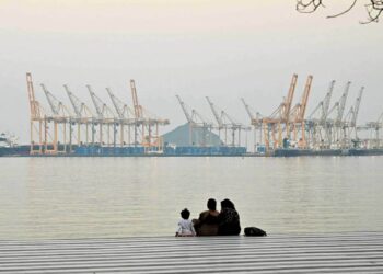 SEBUAH keluarga duduk berlatar belakangkan pelabuhan di luar bandar pantai Fujairah, di Selat Hormuz. - AFP