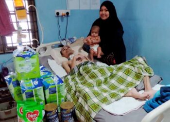 NUR Izzati Farhana Sazali memangku anak sulungnya sambil melihat keadaan Wan Mohd. Amzar Wan Ahmad yang koma di Kampung Lati, Pasir Mas, Kelantan.