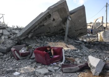SEORANG budak duduk atas kerusi di tepi runtuhan bangunan di Gaza. - AFP