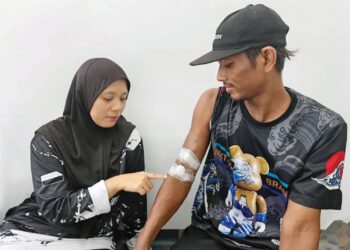 NURUL Bazilah Abdul Wahab (kiri) menunjukkan tapak dialisis 
di lengan Mohd. Ezral Abd. Razak di Kampung Tanjung Gahai, Lipis, Pahang. – UTUSAN/HARIS FADILAH AHMAD